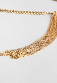 Collier en chaîne dorée mettant en avant une section à maillons épais et un gland en cascade de fines chaînes, créant une apparence texturée.