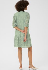 Verhoherkkypuku vaaleanvihreällä kukkakuviolla, kyynärpäähän asti ulottuvilla hihoilla ja polven ylle ulottuvalla pituudella, jossa on kerroksittain oleva hame ja rento istuvuus.