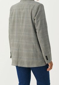 Szary, w kratę marynarka o klasycznym kroju, z pojedynczym rozcięciem, kołnierzem klapowym i czarnymi guzikami, zestawiona z niebieskimi dżinsami.