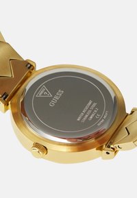 Kultakloroottinen teräksinen kello, jossa on kiiltävä pinta, joka näyttää vedenkestävyysyksityiskohtia ja logon; varustettu turvallisella solkisysteemillä.