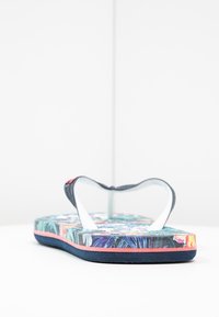 Infradito con una soletta decorata che presenta design tropicali, cinturini in gomma blu navy e un inserto bianco per le dita. Base morbida e testurizzata con accenti rosa.