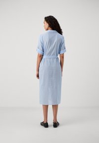 Vestido midi listrado azul claro com mangas curtas dobradas, cintura com cinto e silhueta reta, feito de um tecido macio. Calçado preto visível.