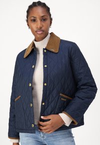 Granatowa pikowana kurtka z brązowym kołnierzem z materiału sztruksowego, złotymi zatrzaskami i kieszeniami. Posiada subtelne logo marki na dolnej kieszeni.