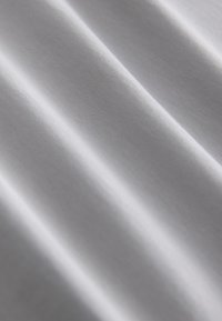 Tissu tissé lisse et léger de couleur blanche douce, présentant une texture subtile et des plis délicats qui créent des ombres douces.