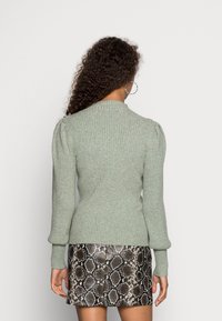 Pull vert clair côtelé avec manches bouffantes, associé à une mini-jupe texturée imprimé serpent. Vue de dos mettant en valeur le design et la coupe.