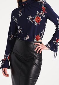 Námořnická halenka s dlouhým rukávem a květinovým vzorem, s volány na manžetách, spárovaná s černou koženou sukní s vysokým pasem.
