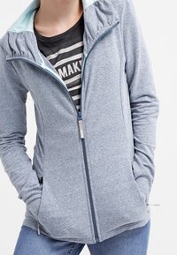 Giacca zip-up azzurro chiaro con colletto alto, realizzata in tessuto morbido, con dettagli a costine e una fodera interna a contrasto per il cappuccio.