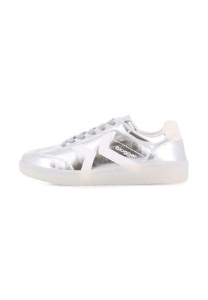 Zapatilla deportiva plateada de caña baja con diseño de chevron blanco, cordones grises y suela translúcida, mostrada de lado sobre fondo blanco.