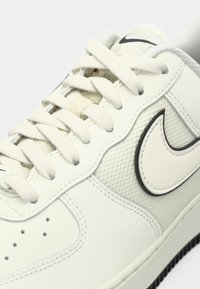 Białe skórzane sneakersy z teksturowanymi akcentami, płaskimi sznurowadłami i logo w kształcie łyżwy z czarnym konturem. Posiadają perforowaną część palców dla wentylacji.