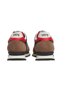 Smeđe nubuk tenisice s crvenim i bijelim akcentima, s retro dizajnom i ispisom "1973" na peti. Crna gumena potplat i pruga.