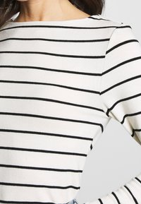 Randig tröja med vit bas och svarta horisontella linjer. Har rund halsringning och ribbade muddar, tillverkad av ett mjukt, texturerat tyg.