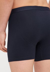 Marineblaue Baumwollboxershorts mit glatter Textur, einem elastischen Bund mit Logo und einer engen Passform, die durch abgerundete Nähte hervorgehoben wird.