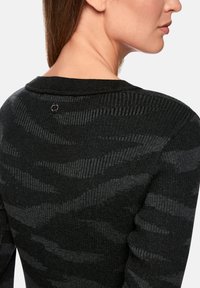 Black sweater with a wavy textured pattern, featuring ribbed accents and a small logo button at the back neckline.