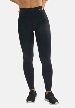 Leggings negros de cintura alta con un tejido suave y elástico. Presentan un diseño ajustado y un detalle del logo en la cinturilla. Combinados con zapatillas negras.