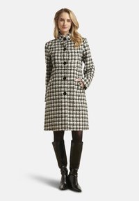 Wollen jas met pied-de-poule-patroon in zwart en wit, voorzien van een hoge kraag, knopen aan de voorkant en zijzakken, gecombineerd met kniehoge laarzen.