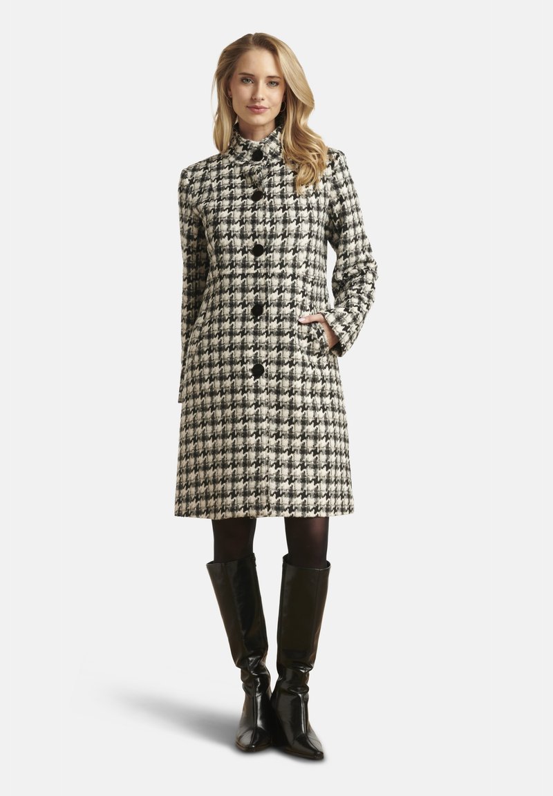 Wollen jas met pied-de-poule-patroon in zwart en wit, voorzien van een hoge kraag, knopen aan de voorkant en zijzakken, gecombineerd met kniehoge laarzen.