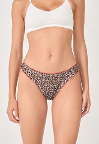 Woman wearing leopard print bikini-style underwear with pink trim and a white crop top against a plain background.