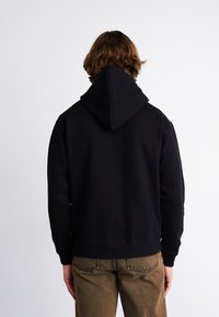 Zwarte hoodie van katoen, met een comfortabele pasvorm en ribbelmanchetten, gecombineerd met lichtbruine textuurbroek.