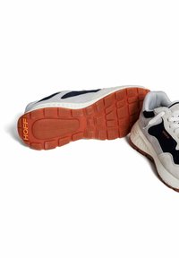 Des chaussures de sport avec une tige grise et marine, des accents blancs et une semelle en caoutchouc orange texturée. Nom de la marque "HOFF" en orange sur le côté.