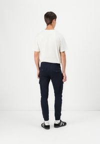 Vit t-shirt med kort ärm, marinblå cargobyxor med sidofickor, slim fit, ribbad mudd och svarta sneakers med vita detaljer.