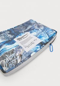 Blå mönstrad laptopfodral med en slät yta, som har olika mönster och texturer. Inkluderar en vit etikett med varumärkesinformation.