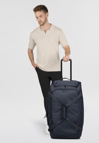 Sac de voyage marin avec double fermeture éclair, sangles ajustables et poignée télescopique. Présente une forme rectangulaire et une texture de tissu durable.