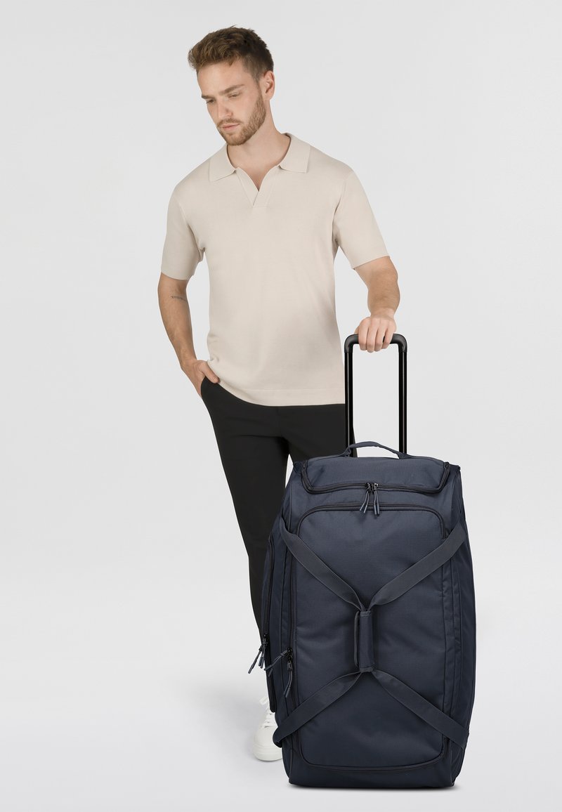 Sac de voyage marin avec double fermeture éclair, sangles ajustables et poignée télescopique. Présente une forme rectangulaire et une texture de tissu durable.