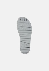 Semelle en caoutchouc grise avec des motifs texturés, y compris des rainures et des lignes ondulées. Taille indiquée comme 38, détail de logo circulaire présent.