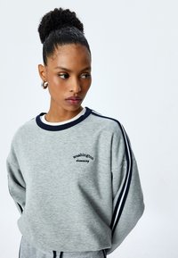 Grijze sweatshirt met marineblauwe accenten, ronde halslijn en oversized pasvorm. Heeft de tekst "Washington dreaming" geborduurd op de voorkant.