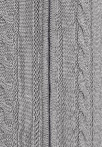 Gros plan sur un tissu gris en maille avec des motifs de torsades verticales et de côtes, mettant en valeur la texture et les détails du tissu.