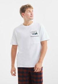 Witte katoenen t-shirt met een zak en een kleurrijke olifantgrafiek, korte mouwen en een relaxte pasvorm.