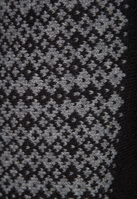 Textil med ett geometriskt mönster i nyanser av svart och grått, som visar en stickad textur med fint detaljerade och subtila djup.