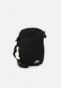 Mala tiracolo preta da Nike com alça ajustável, bolso frontal com fecho de correr e logótipo branco da Nike no canto inferior direito.