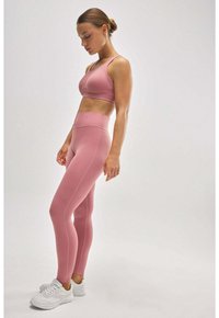 Sujetador deportivo de color rosa claro y leggings a juego, elaborados en una tela suave, con una cinturilla alta y un diseño minimalista. Zapatillas deportivas blancas.