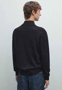 Schwarzer Strickpullover mit einem gerippten Kragen und Bündchen, lockerer Passform und nahtlosen Schultern. Die Rückansicht zeigt eine glatte Textur.