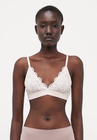 Lace bralette in light beige with a triangular shape, scalloped edges, and thin straps. Soft fabric with a smooth underband.