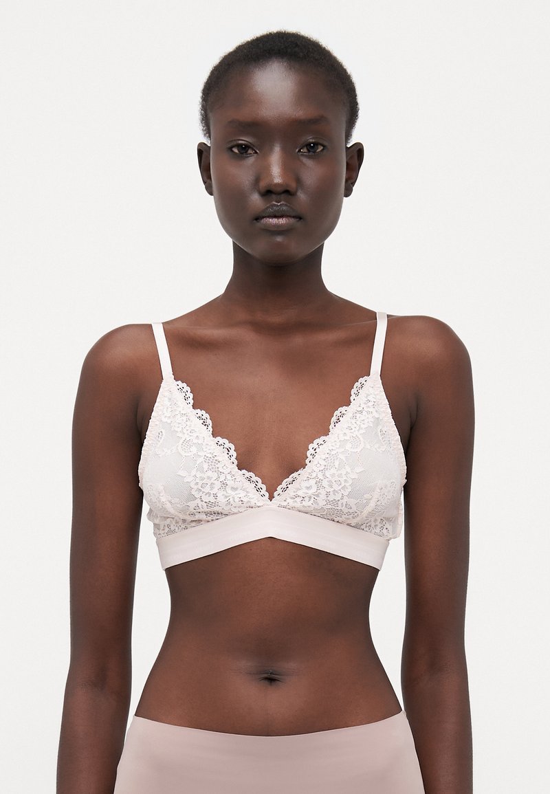 Lace bralette in light beige with a triangular shape, scalloped edges, and thin straps. Soft fabric with a smooth underband.