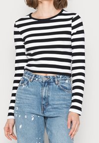 Svartvit randig långärmad crop top i bomull; kombinerad med högmidjade slitna blå jeans.