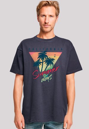 Navy blue cotton t-shirt featuring a large graphic with palm trees, a sunset gradient triangle, and the text "California Summer days" in vibrant colors.