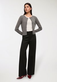 Szary sweter z dzianiny z perełkowymi akcentami, noszony na białej bluzce, w połączeniu z czarnymi spodniami w pionowe paski z wysokim stanem oraz burgundowymi, spiczastymi butami.