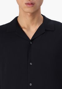 Camisa negra de manga corta con una textura suave y lisa, cuello y cierre delantero con botones negros.