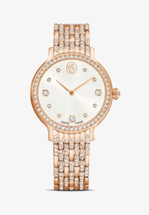 Montre en or rose avec un boîtier rond, des accents ressemblant à des diamants autour de la lunette et un bracelet texturé à plusieurs brins. Cadran blanc avec aiguilles dorées.