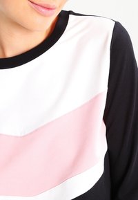 Färgblöckt sweatshirt med horisontella ränder i svart, vitt och mjuk rosa, med rund halsringning och ribbade muddarna. Slät textur.