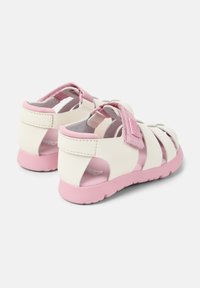White and pink sandals featuring a closed-toe design, adjustable strap, and rubber sole. The upper has cut-out detailing for ventilation.