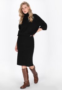 Schwarzer, gestrickter Pullover mit Rollkragen, kombiniert mit einem schwarzen, gerippten Midirock und braunen, kniehohen Lederstiefeln mit Akzentbeschlägen.