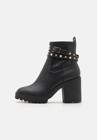 Boots negre din piele, până la gleznă, cu un toc chunky, curea decorativă cu studs, vârf rotund și suprafață texturată. Dispune de un tab de tracțiune sub formă de buclă în spate.