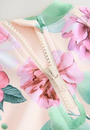 Lähivõte valgest lukust, mis on osaliselt avatud lillelise mustriga kangal, kus on roosad lilled ja rohelised lehed.