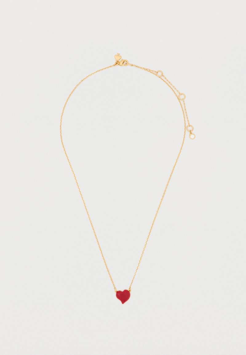 Zlatý náhrdelník s malým červeným príveskom v tvare srdca, jemným reťazcom a nastaviteľnou dĺžkou, doplnený drobným kruhovým detailom.