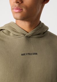 Olijfgroene hoodie van zachte stof, met een voorvak in kangoeroestijl en geborduurd "MARC O'POLO DENIM" logo in het zwart.