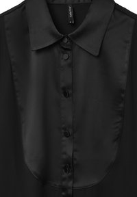 Chemisier en satin noir avec un col, un devant à boutons et une texture lisse. Présente un patch contrastant au niveau de la poitrine.